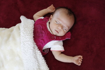 Un bébé en robe rose dort sous une couverture blanche
