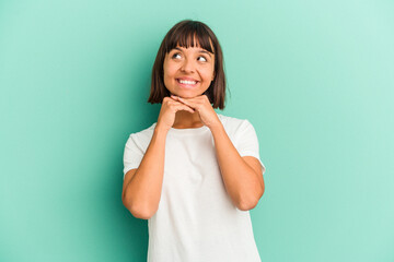 Young mixed race woman isolated on blue keeps hands under chin, is looking happily aside.