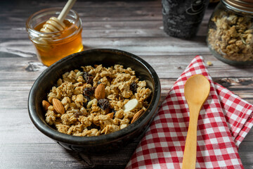 Normal view of a bowl with served granola and honey on a wooden table with a spoon. Healthy and natural eating concept.