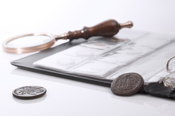 Numismatics. Old collectible coins and a magnifying glass on the table.