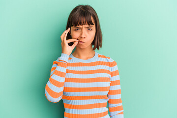 Young mixed race woman isolated on blue with fingers on lips keeping a secret.