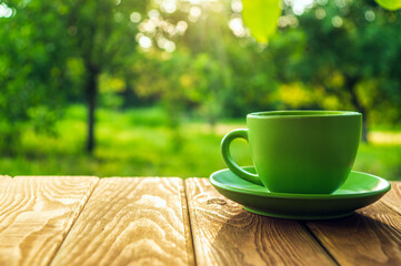 Green cup of hot coffee on a wooden table in a green garden in the morning or evening. Summer background