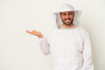 Young apiculture caucasian man isolated on white background showing a copy space on a palm and holding another hand on waist.