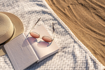 Summer vacation on the beach on the sand. On a white towel book glasses and a hat.