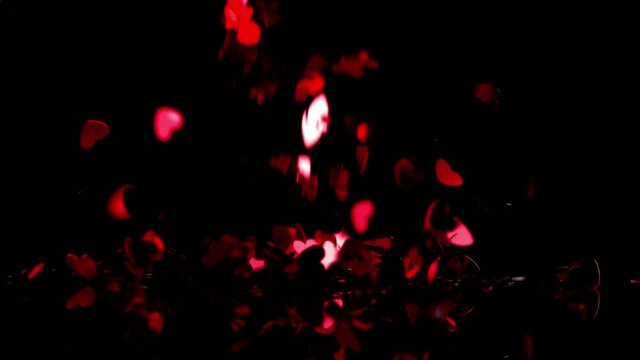 Animation of red kaleidoscope shapes and red hearts falling on black background