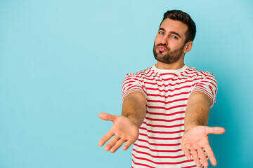 Young caucasian man isolated on blue background folding lips and holding palms to send air kiss.