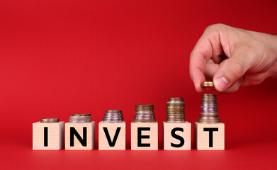 Wooden cubes with the inscription "invest" with a hand with money on a red background. Wooden cubes with letters. Money accumulation concept