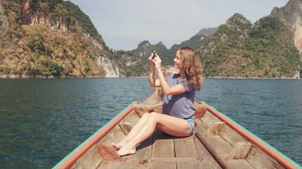 Fototapeta na wymiar Young Happy Mixed Race Girl Sitting and Relaxing on Traditional Thai Wooden Long Tail Boat at Khao Sok Lake. Phang Nga Province, Thailand.