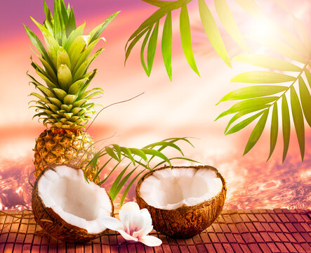 Coconut, pineapple fruits and magnolia flower on sea or ocean background with palm trees and sunset rays, tropical Caribbean or Hawaiian paradise, summer tourism and travel, beach vacation concept.