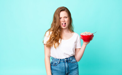 pretty red head woman feeling disgusted and irritated and tongue out and holding a breakfast bowl