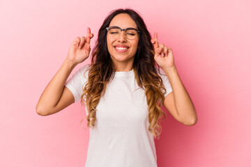 Young mexican woman isolated on pink background crossing fingers for having luck