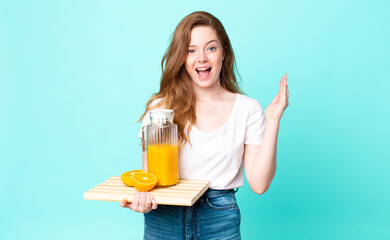 pretty red head woman feeling happy and astonished at something unbelievable and holding an orange...