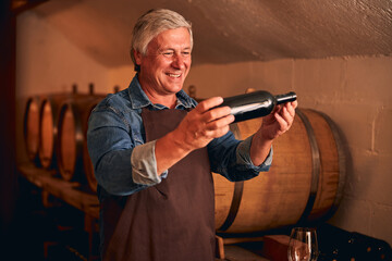 Cheerful man with bottle of wine standing in wine cellar