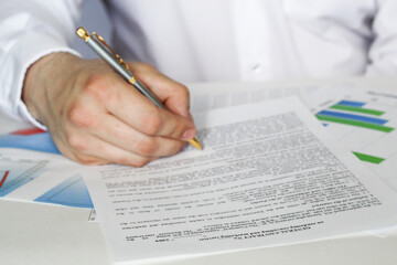 A businessman sitting at an office desk signs a contract with a shallow emphasis on signing....
