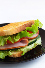 close-up toasted homemade sandwich with fresh vegetables on the black plate.tasty sandwich with ham, green salad, cucumbers and tomatoes on the white background.copy space. vertical