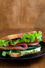 tasty sandwich with ham, green salad, cucumbers and tomatoes on the wooden background.toasted...