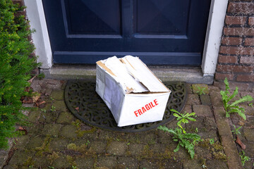 Damaged delivery cardboard box at front door of a house, Fragile package with dents, bad delivery...