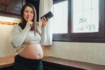 Hispanic pregnant woman asking for silence while recording audio on cell phone.
