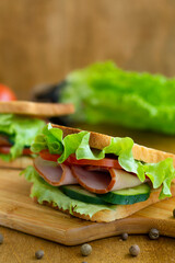 close up toasted homemade sandwich with fresh vegetables on the brown cutting board.two tasty sandwiches with ham, green salad, cucumbers and tomatoes on the wooden background.vertical.copy space