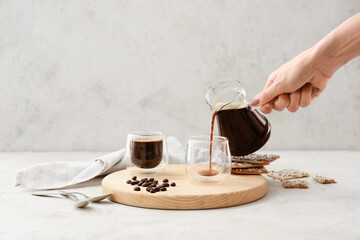 Woman pouring coffee from pot into cup on light background