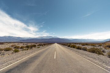 two lane road in a arid landscape in Argentina leading to mountains against blue sky