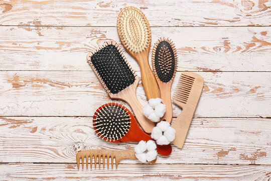 Composition with hair brushes, combs and cotton flowers on light wooden background