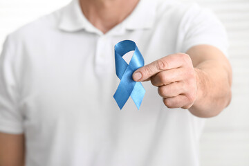 Man with blue ribbon on light background, closeup. Colon cancer concept