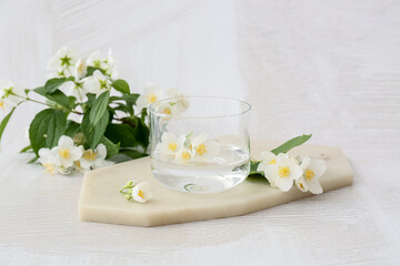 Composition with beautiful jasmine flowers and glass of water on light background