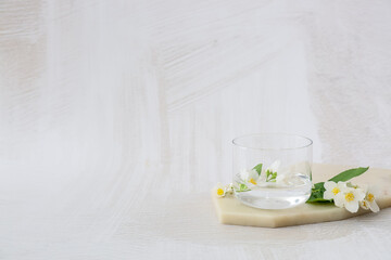 Composition with beautiful jasmine flowers and glass of water on light background