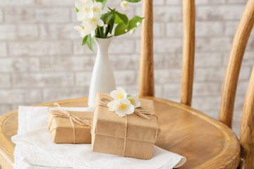 Gift boxes and beautiful jasmine flowers on chair against brick wall