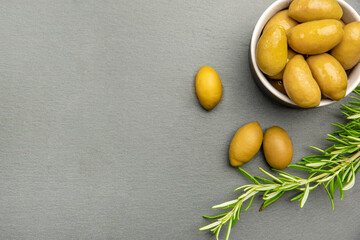 Green olives. Bella di cerignola Italian olives. Colored olives and a sprig of rosemary lie on a black stone countertop. Culinary banner or poster for advertising with place for text