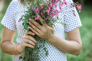 a girl in a white light dress holds a bouquet of wild flowers in her hands. depersonalized photo, midsection, copy space, selective focus