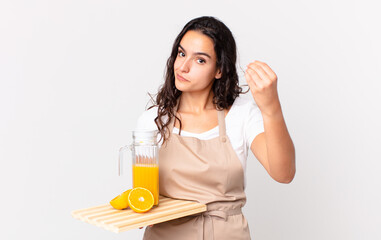 hispanic pretty chef woman making capice or money gesture, telling you to pay and holding an orange...