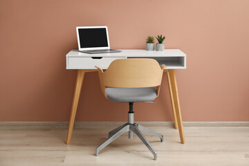 Stylish workplace with laptop and comfortable chair near beige wall indoors. Interior design