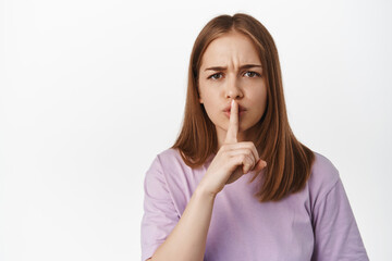 Fototapeta premium Close up portrait of angry girl hushing, frowning upset and shushing, shhh gesture, tell to keep quiet, scolding loud person, standing against white background