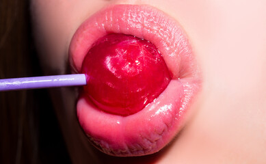 Licking candy. Lollipop model. Woman lips sucking a candy. Glamor sensual model with red lips eat...