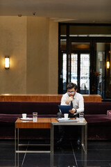 Vertical wide angle view at successful businessman working in hotel lobby, copy space