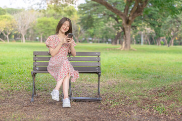 Young and beautiful Asian woman using her smartphone while resting in the park