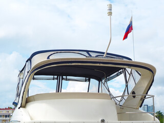 Fototapeta na wymiar The upper part of the yacht with the tricolor Russian flag against the blue sky with clouds