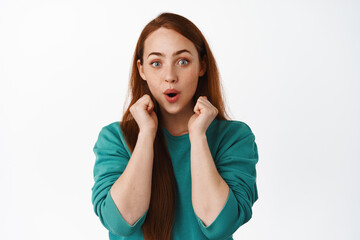Fototapeta premium Excited and amused redhead woman hear stunning news, look in awe at something super cool, listening with excitement, say wow, standing over white background
