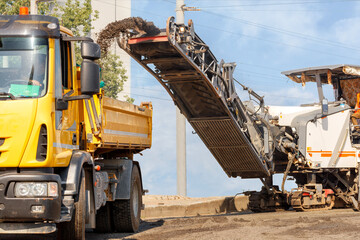 The road milling machine removes the top layer of asphalt from the road section and loads it onto the tipper.