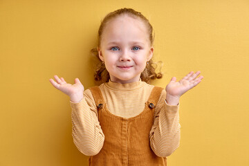 Cute little girl doubting and shrugging shoulders in questioning gesture, isolated in studio, copy...