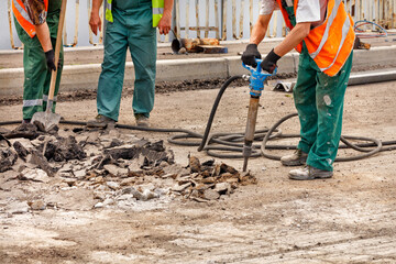A team of road workers are repairing a section of road by smashing old asphalt with a pneumatic...
