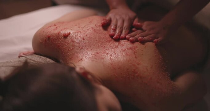 Professional massagist applying and rubbing pink organic scrub on back of woman. Natural luxury cosmetics used in bodycare wellness spa resort 4k footage