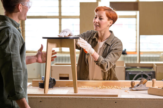 Two skilled talented carpenters making wooden chair in workshop, team work, young caucasian man and woman engaged in woodworking, discussing, sharing ideas while working