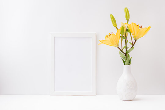 Home interior with decor elements. Mockup with a white frame and yellow lilies in a vase on a light background