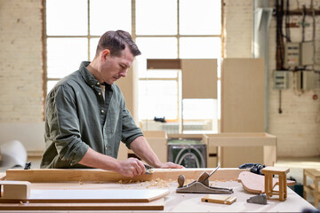 Busy and serious joiner is working with wood using tools. Professional carpenter in joiner's shop. Concept of woodworking and craftsmanship. side view portrait