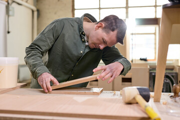 male joiner comparing the length and width of wooden material while woodworking, handsome guy carpenter is focused on work, in workshop. handmade furniture by professional carpenter