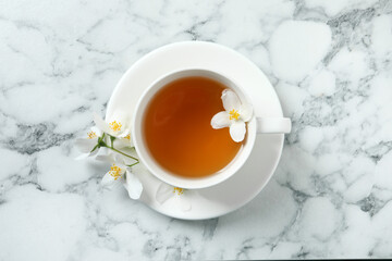 Cup of aromatic jasmine tea and fresh flowers on white marble table, top view