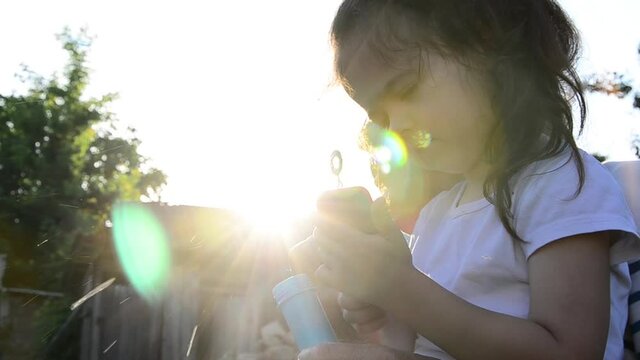 Child blowing soap bubbles at sunset. Happy child in summer. A little girl with her grandmother plays with soap bubbles. The old grandmother and her granddaughter are playing merrily. Baby concept